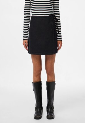 Zwarte denim wikkelrok met een strik in de taille, gecombineerd met een zwart-wit gestreept shirt met lange mouwen en zwarte leren laarzen tot aan de knie.