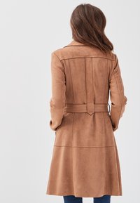 Brown faux suede long coat with a belted waist, back yoke seam, and vertical pleats, featuring a tailored fit and smooth texture.