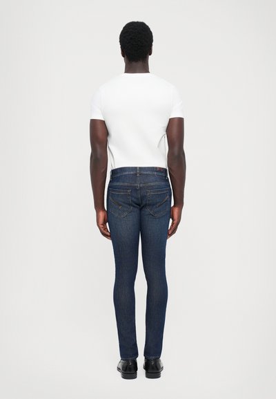 Jeans skinny blu scuri con cinque tasche, cuciture a contrasto e vita media, abbinati a una semplice t-shirt bianca a maniche corte.