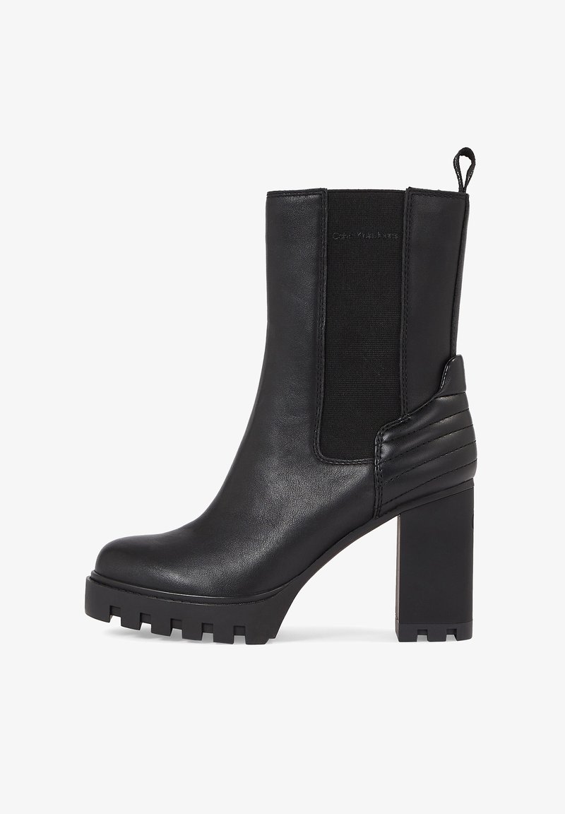 Czarny skórzany botek sięgający kostki na masywnej podeszwie, z elastycznymi bocznymi panelami, żebrowanymi akcentami i teksturowaną gumową podeszwą.
