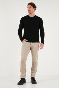 Maglietta nera a maniche lunghe in maglia a costine abbinata a pantaloni chino beige e sneakers nere, caratterizzata da una silhouette aderente e scollo tondo.