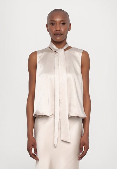 Blouse en soie taupe sans manches avec un nœud au cou, présentée dans une coupe décontractée et une texture lisse, accompagnée d'une jupe assortie.