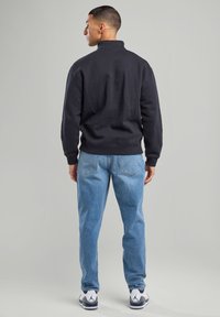 Black sweatshirt with a high collar, paired with light blue jeans. Features include ribbed cuffs and hem, and sporty white and gray sneakers.