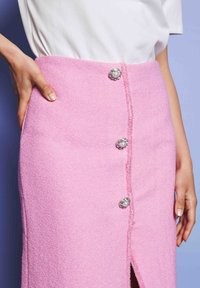Ροζ υφασμάτινη φούστα με μπροστινή σχισμή, διακοσμημένη με διακοσμητικά κουμπιά με πέρλες και ασημένιες λεπτομέρειες. Ραφή κατά μήκος.