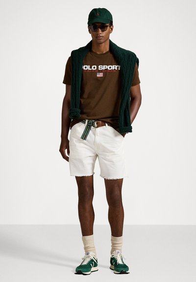 Camiseta marrón con el logo "POLO SPORT", pantalones cortos blancos, suéter de punto verde drapeado, gorra verde, gafas de sol y zapatillas verdes con suelas blancas.