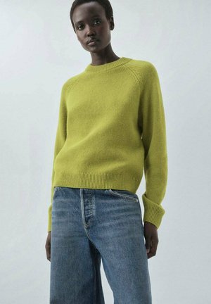 Green knit sweater with ribbed cuffs and hem, paired with light blue wide-leg jeans, featuring a soft texture and crew neckline.