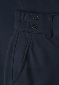 Close-up of dark navy trousers with a double-button waistband, belt loop, and side pocket visible on smooth fabric.