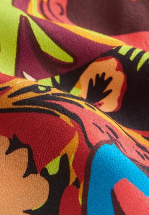 Colorful fabric with vibrant floral patterns in red, orange, green, and blue. Textured surface, soft drape, and bold design elements.