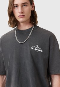 T-shirt gris surdimensionné en coton, avec un logo imprimé en blanc sur la poitrine et un col rond. Comprend un collier en chaîne argentée.
