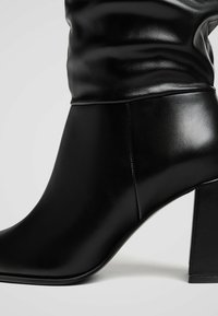 Stivaletto in pelle nera alla caviglia con punta arrotondata, tomaia morbida e tacco quadrato spesso. Presenta una texture liscia e cuciture pulite.