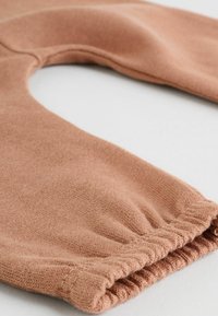 Zacht, roestkleurig stof met een gladde textuur en elastische manchetten. Het ontwerp heeft een ronde halslijn en een ontspannen pasvorm.