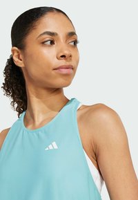 Tricou sportiv de culoare albastru deschis, fabricat dintr-un material texturat, având un logo alb. Are un decolteu rotund și un design fără mâneci.