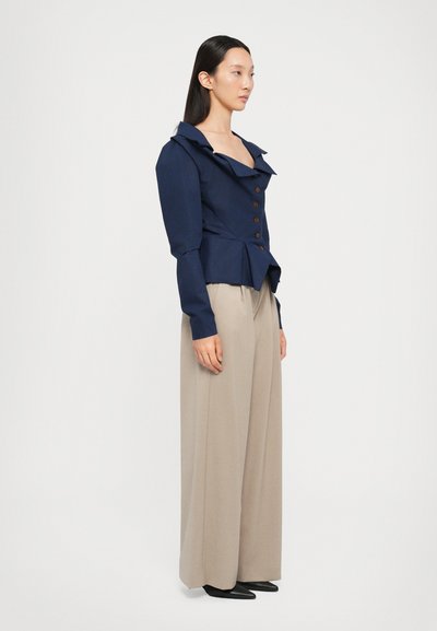 Navy blue fitted jacket with a pointed collar and button closure; paired with beige wide-leg trousers and black shoes.