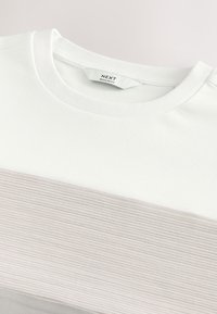 T-shirt blanc à col rond avec une bande horizontale côtelée gris clair sur la poitrine et une étiquette « NEXT Regular Fit » à l'intérieur du col.