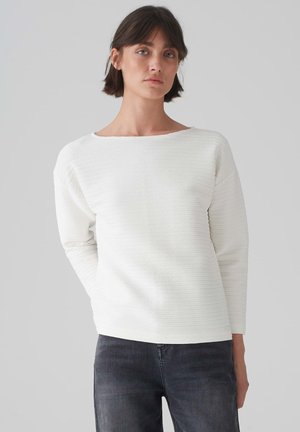 White textured sweater with a round neckline and long sleeves, featuring horizontal ribbed patterns and a relaxed fit. Paired with dark jeans.