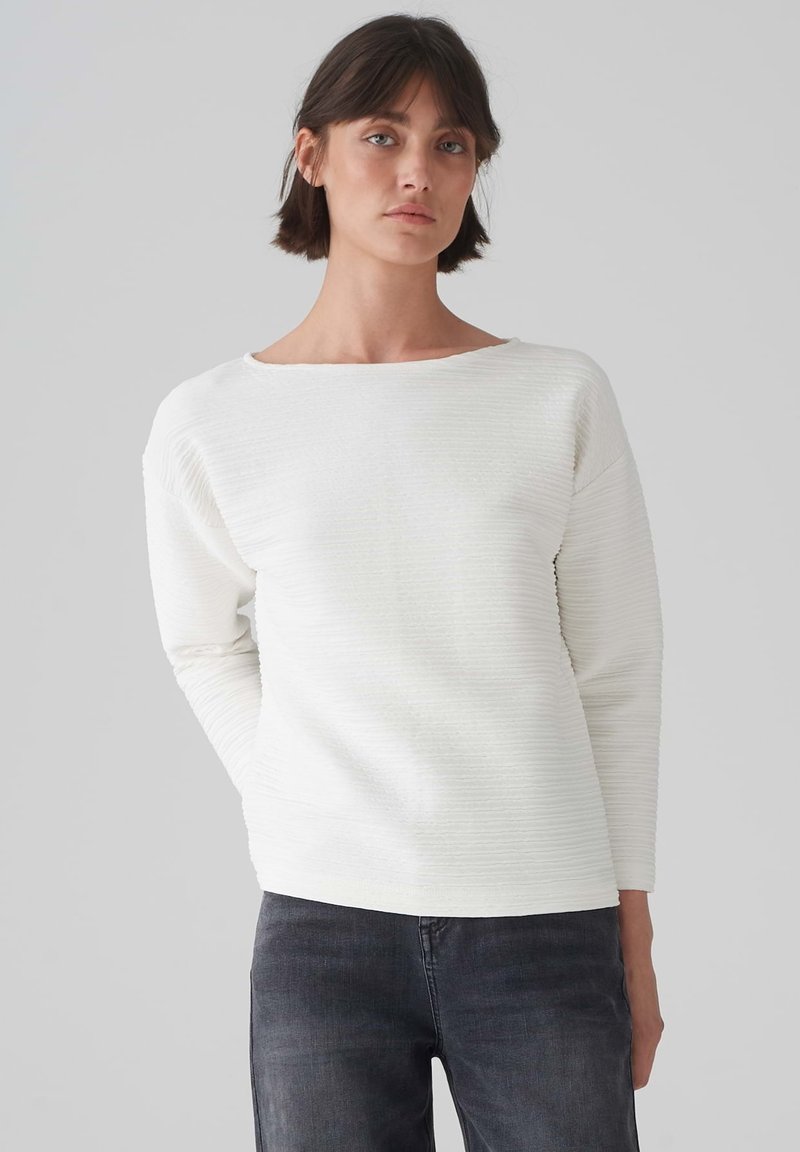 Maglione bianco a trama con scollo rotondo e maniche lunghe, caratterizzato da motivi a coste orizzontali e una vestibilità comoda. Abbinato a jeans scuri.