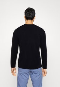 Schwarzes Langarmshirt mit Rundhalsausschnitt und glatter Textur, kombiniert mit hellblauen Hosen. Die Rückansicht zeigt minimale Details.