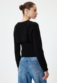Schwarzer Rippstrickpullover mit einem cropped Design und langen Ärmeln, kombiniert mit hellblauen hochgeschnittenen Jeans. Verfügt über ein einzigartiges geschichtetes Rückendetail.