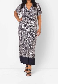 Maxi sukienka w granatowo-kremowym kolorze z kwiatowym wzorem, dekoltem w serek, krótkimi rękawami, wcięciem w talii oraz jednolitą granatową falbaną. Noszona z czarnymi sandałami na paski.