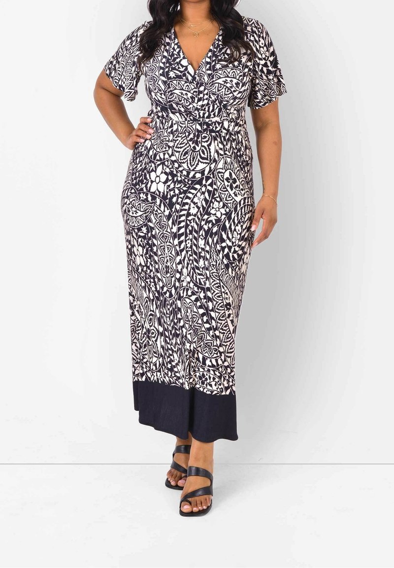 Maxi sukienka w granatowo-kremowym kolorze z kwiatowym wzorem, dekoltem w serek, krótkimi rękawami, wcięciem w talii oraz jednolitą granatową falbaną. Noszona z czarnymi sandałami na paski.