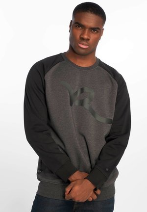 Grå sweatshirt med sorte raglanærmer, prydet med et stort mørkt logo på forsiden, struktureret stof, og ribbede manchetter og kant.