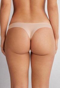 Nude stringtrosor med en sömlös design, mjukt elastiskt midjeband och en slät finish, som ger minimal täckning och ett strömlinjeformat utseende.