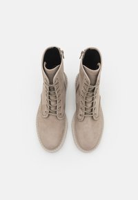 Beige semskede ankelstøvler med snøringsdesign, front- og sideglidelås, og teksturert gummisåle. Ren, minimalistisk estetikk.