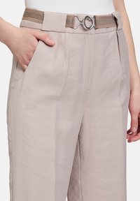 Světlé béžové kalhoty s bočními kapsami a širokým pasem, doplněné texturovaným hnědým páskem a dekorativní sponou ze stříbra.