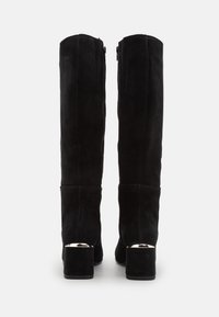Botas altas de ante negro hasta la rodilla con tacón cuadrado y acento metálico en el tacón; cuenta con una cremallera lateral. Textura lisa en toda la superficie.