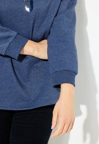 Sweat à capuche bleu à coupe décontractée, doté d'un col rond et d'un tissu texturé. Des sequins décoratifs forment un motif sur la poitrine.