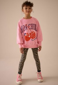 Pink sweatshirt med kirsebær grafik og tekst, kombineret med leopardprint leggings og lyserøde sneakers med hvide snørebånd.