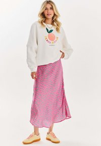 Bílá mikina s broskvovým grafickým vzorem a textem, spárovaná s růžovou sukní s puntíky a žlutými teniskami, vyrobená z měkkého materiálu a s volným střihem.