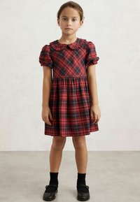 Röd och marinblå rutig klänning med puffärmar, en volangkrage och en samlad midja. Matchas med svarta skor och strumpor.