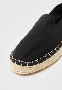 Espadrille en toile noire avec semelle intermédiaire en corde de jute et coutures contrastées. Bout arrondi avec conception de talon ouvert.