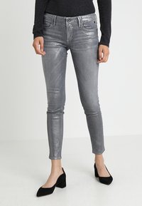 Jeans ajustados de color gris metálico con una textura suave, diseño de cinco bolsillos y un brillo sutil. Combinados con tacones puntiagudos negros.