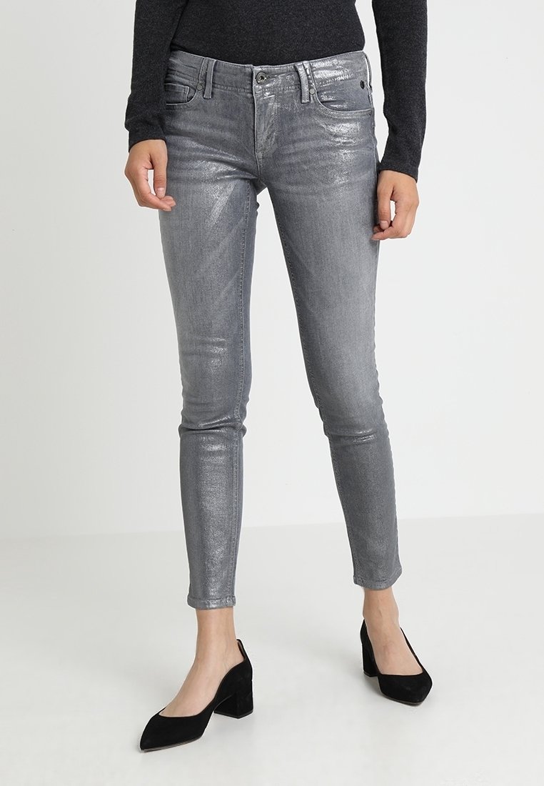 Jeans ajustados de color gris metálico con una textura suave, diseño de cinco bolsillos y un brillo sutil. Combinados con tacones puntiagudos negros.