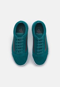 Teal suede sneakers with brown leather accents, white rubber soles, six eyelet lace-up design, and textured fabric details on the upper.