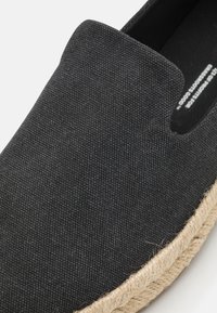 Scarpe slip-on nere in canvas con tomaia testurizzata e suola in corda di juta naturale. Presentano una punta arrotondata e sottili dettagli di cucitura.