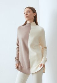 Knit turtleneck sweater with a split design, featuring beige and cream sections, ribbed cuffs, and side slits for ease of movement.