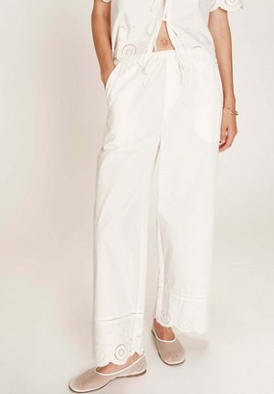 Pantalons blancs amples avec un ourlet à volants brodé, dotés d'une taille élastique et de poches latérales. Associés à des chaussures à enfiler.