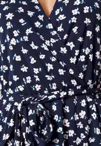 Laivastonsininen kukkakuosiset wrap-mekko, jossa on pieniä valkoisia ja vaaleansinisiä kukkia, pehmeä kangas ja vyötäröä korostava solmittava vyö.