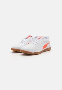 Weiße Sportschuhe mit orangefarbenen Akzenten, Gummisohle, glatter Textur und Schnürverschluss. Auffälliges Design mit Logo an der Seite.