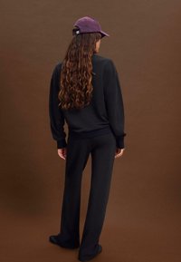 Felpa nera con maniche lunghe, abbinata a pantaloni neri coordinati. Un cappello viola completa il look, con visiera curva e retro regolabile.