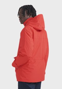 Rote Parkajacke mit Kapuze, tailliertem Schnitt und strukturiertem Stoff. Beinhaltet ein Logo am Ärmel und seitliche Taschen.