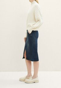 Jersey de canalé crema, falda lápiz de mezclilla oscura con abertura lateral y zapatos beige sin cordones con suelas gruesas. Conjunto sencillo y casual.