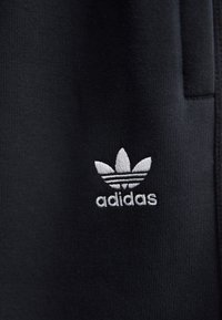 Black fabric with a ribbed texture features a white embroidered Adidas logo, including three leaf-like stripes above the brand name.