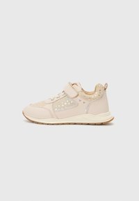Des chaussures de sport beiges avec une tige texturée, ornées de motifs en forme de cœur dorés et d'une sangle velcro ; semelle en caoutchouc pour traction et stabilité.