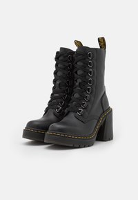 Black leather lace-up ankle boots with thick block heels and yellow stitching along the sole edge, set against a white background.