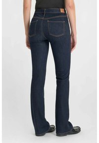 Donkerblauwe spijkerbroek met flair en hoge taille, oranje stiksels, twee achterzakken en een leren merkembleem op de tailleband.