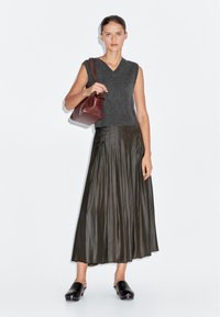 Šedý bezrukávový pletený top, skládací tmavozelená midi sukně, hnědá kabelka a černé dřeváky se stříbrnými akcenty, na bílém pozadí.